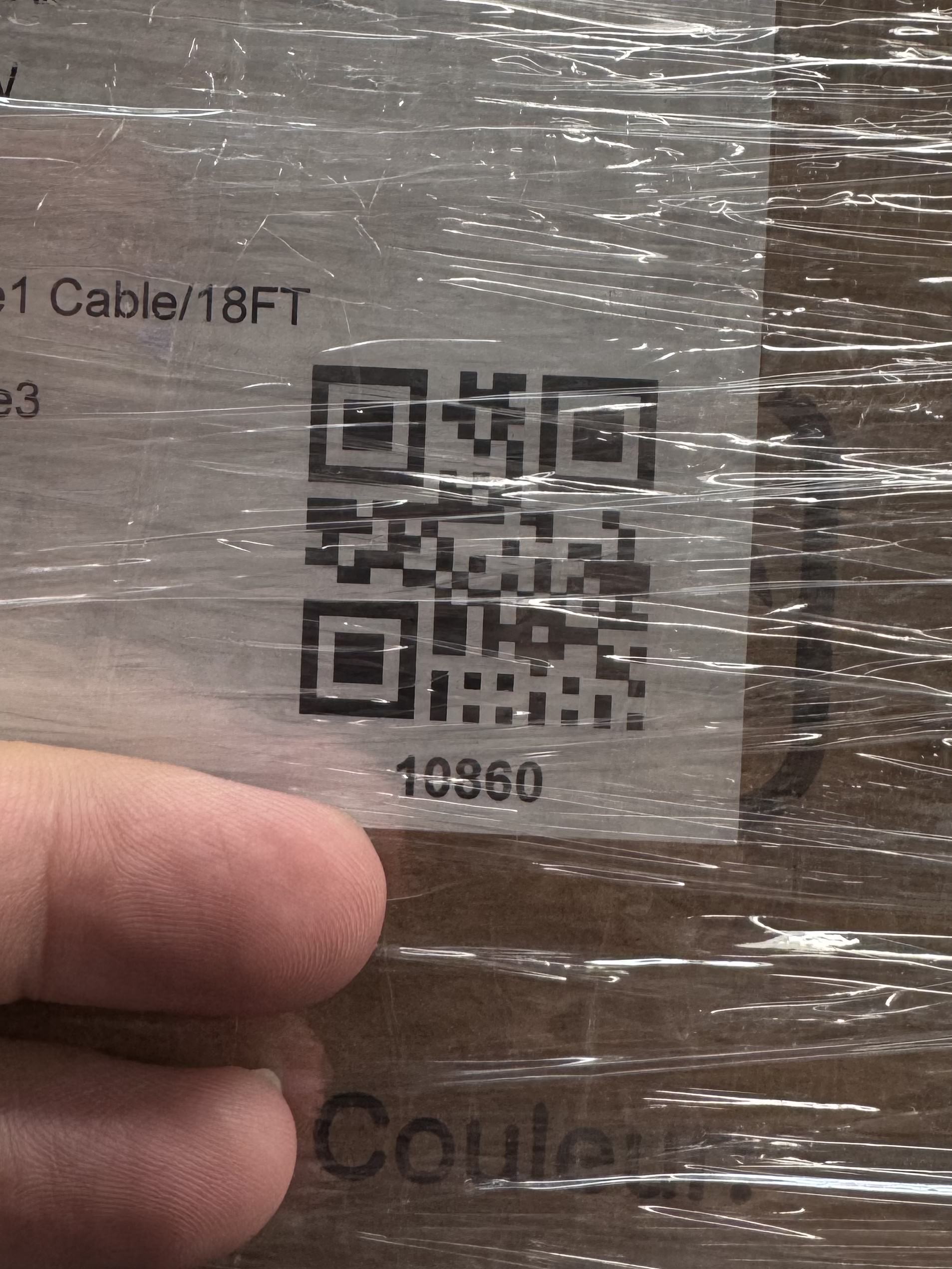 Macro photo of a QR-coded shipping label under wrinkled stretch film — the specular streaks across the wrap are exactly what clips the sensor to white